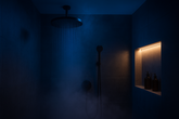 A modern rainfall shower setup in a dimly lit bathroom, featuring a black ceiling-mounted showerhead, handheld sprayer, LED-lit niche with bottles, and soft steam creating a relaxing spa-like ambiance.